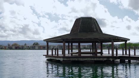 Wooden-gazebo-by-the-lake-and-neighborhood-in-the-background