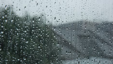 Rain-drops-on-clear-glass-window-cascading-down,-close-up-static-shallow-depth-of-focus