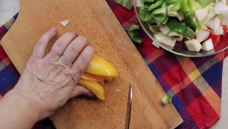 Overhead-view-of-woman's-hands-using-a-knife-to-slice-yellow-sweet-pepper-on-a-cutting-board-and-adding-it-to-a-bowl