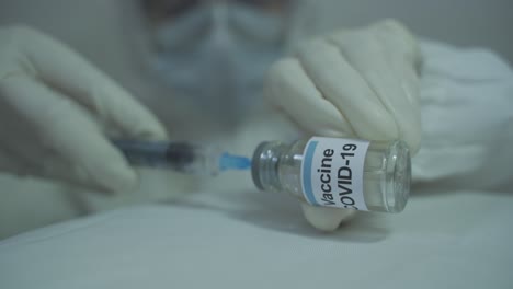 human-wearing-protective-PPE-kit-carefully-initiating-to-draw-out-covid-19-vaccine-from-vial-into-syringe-in-horizontal-position