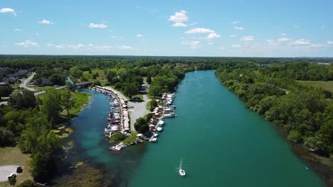 Ascending-Aerial-backwards-shot-of-niagara-river-with-luxury-boats-at-pier,driving-cars-on-street-and-green-forest-landscape-in-Canada
