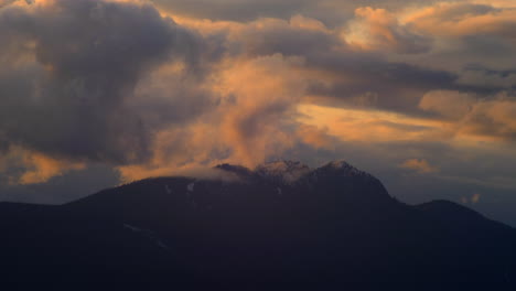Clouds-rolling-over-the-mountain-peak-during-sunset---time-lapse