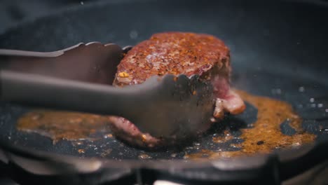 Chef-moves-a-steak-in-circular-movements-with-tongs-through-a-frying-pan