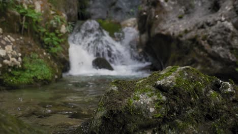 Nahaufnahme-Eines-Felsens-Im-Bach-Mit-Wasserfall-Im-Hintergrund