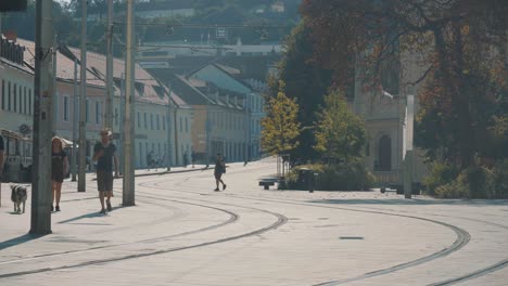 Menschen,-Die-Auf-Einer-Straße-Mit-Straßenbahnschienen-Und-Der-Bratislavaer-Burg-Im-Hintergrund-In-Der-Slowakei-Spazieren