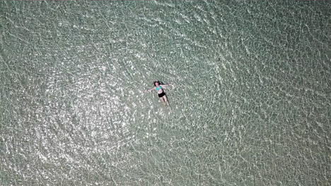 AERIAL-LOWERING-shot-towards-a-teenage-girl-lying-in-shallow-water