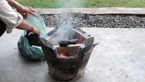 Person-adding-charcoal-to-traditional-Thai-clay-stove-hot-fire---Thailand-food