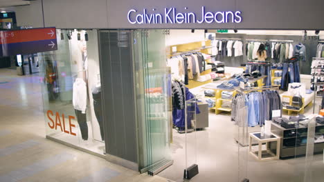 People-walk-by-Calvin-Klein-Jeans-store-in-mall,-slomo-from-above
