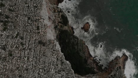 4k-Aerial-view-of-a-rock-cliff-with-waves-and-green-water-sea-in-Denia,-Alicante,-Spain,-wide-angle-backward-shot