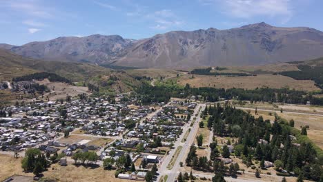Pan-left-flying-above-Esquel-village-surrounded-by-trees-and-Andean-mountains,-Patagonia-Argentina