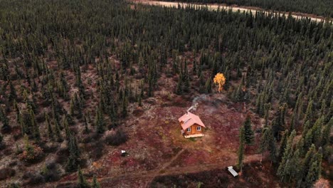 Vista-Aérea-De-Una-Casa-Aislada-Con-Chimenea-Humeante-En-Un-Bosque-De-Coníferas-De-Alaska
