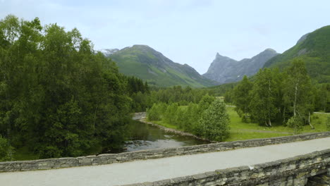 Stone-Bridge-Over-The-Calm-River-With-A-View-Of-The-Alpine-Mountains-In-Norway