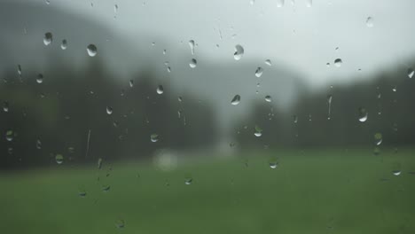 Rain-drops-on-window-glass-with-blurry-nature-background,-static-shot