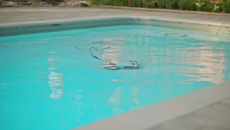 Electric-Pool-Cleaning-Robot-Cleans-Across-Swimming-Pool-Floor-with-Power-Cable-Floating-in-Clear-Reflective-Water