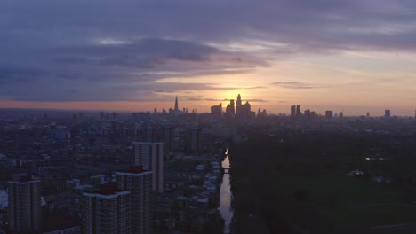 telephoto-dolly-back-Aerial-drone-shot-of-London-Canal-towards-city-skyline-at-sunset