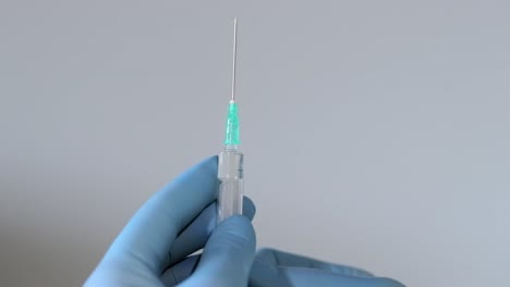 Extreme-close-up-shot-of-doctor's-hands-wearing-surgical-gloves-and-squirting-air-from-syringe-through-a-sharp-needle-on-a-isolated-background