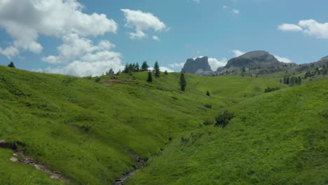 Lush-green-valley-with-small-mountain-stream,-Dolomites-Italy,-aerial