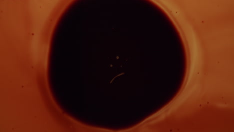 Top-shot-of-an-amber-liquid-forming-abstract-forms-and-shapes-in-the-middle-of-a-black-circle