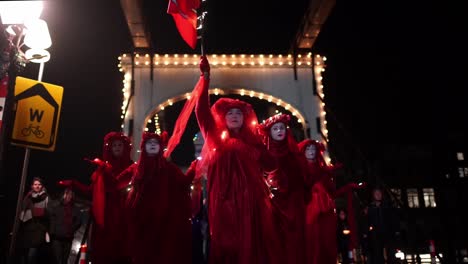 Red-rebels-with-Dutch-Friends-Of-The-Earth-In-Red-Dress-Marching-In-The-Street-At-Night---Climate-Change-Protest-against-Shell-In-The-Hague-and-Amsterdam,-Netherlands---Extinction-rebellion