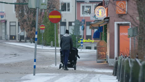 A-man-with-a-stroller,-pram-walks-down-a-slush-covered-street-in-a-Swedish-town,-during-the-covid-19-pandemic