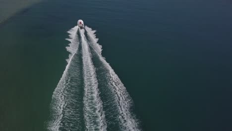Chase-aerial-as-white-speed-boat-splashes-wake-in-shallow-green-lagoon