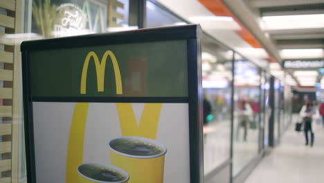 Close-view-of-sign-outside-McDonald's-as-people-walk-behind,-slomo