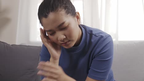 Asian-woman-wearing-a-blue-shirt-sitting-on-a-sofa-feeling-very-headache