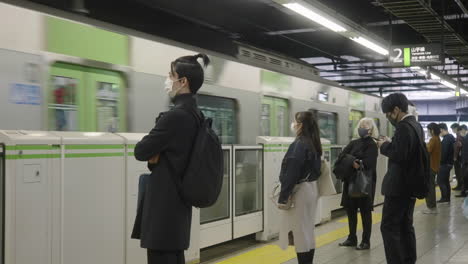 Der-Zug-Nähert-Sich,-Während-Japanische-Pendler-Während-Einer-Pandemie-Auf-Dem-Bahnsteig-Der-Yamanote-Linie-In-Tokio,-Japan,-Warten