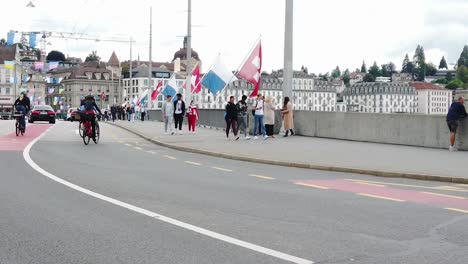 Menschen,-Die-Auf-Der-Straße-Der-Stadt-Luzern-Spazieren,-Mit-Fahnen-Und-Alten-Gebäuden-Im-Hintergrund