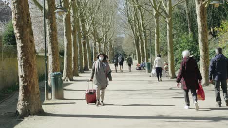 Slow-motion-of-a-young-masked-student-woman-walking-with-luggage-in-the-park-during-Coronavirus-pandemic