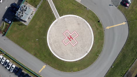 Aerial-Overhead-View-of-a-Helipad-at-a-Hospital,-Drone-Rising-Spin-Shot-on-a-Sunny-Day