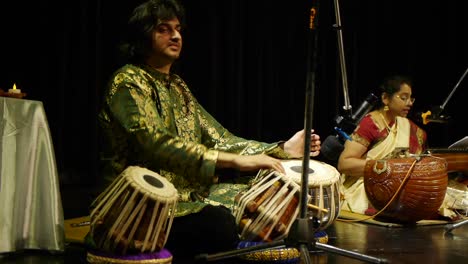 Indian-man-dressed-in-traditional-Indian-silk-clothing-tapping-tablas-with-his-fingers-on-stage
