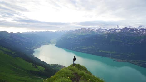 Male-hiker-at-viewpoint-over-lake-Brienz,-stunning-vista-of-snowy-Alps