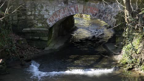Water-flowing-under-a-small-stone-and-brick-bridge