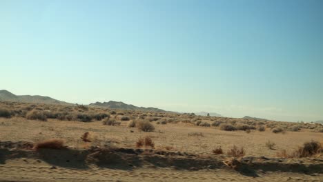 Ich-Fahre-Schnell-Eine-Unbefestigte-Straße-Mitten-In-Der-Wüste-Entlang,-In-Der-Ferne-Berge-Und-Vorbeiziehende-Trockene-Sträucher