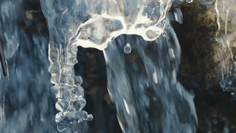 icicle-in-a-frozen-river-with-flowing-water-in-background,-close-up,-slow-motion