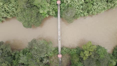 Aerial:-People-walk-across-narrow-jungle-river-on-suspension-bridge