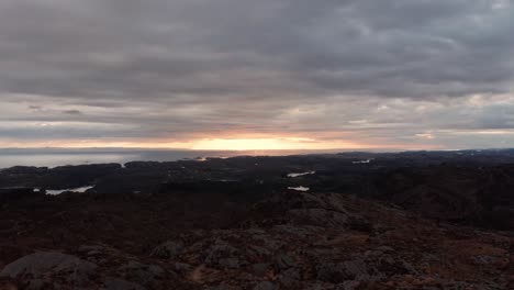 Norway-coastline-at-dawn---Reverse-aerial-with-cloudy-sunset---North-sea-in-background-with-dark-mountain-landscape-in-front