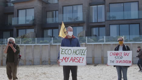 Local-Protesters-holds-signs-in-Eco-Outrage-at-beach-front-of-Carbis-Bay-Hotel-Location-for-G7-Summit,-Cornwall