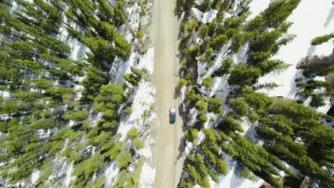 Drone-pulls-away-from-Jeep-wrangler-driving-through-snowy-mountains,-solo-adventure-road-trip