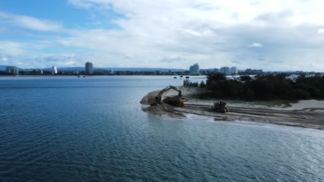 Panning-view-over-water-of-large-machinery-working-on-a-sand-island-creating-a-new-city-harbor
