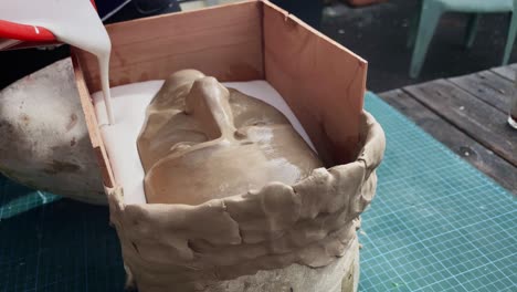 Artist-Crafting-A-Face-Mould-By-Delicately-Casting-Liquid-Plaster-Mix-On-A-Wooden-Framed-Portrait-Bust---Close-Up-Handheld
