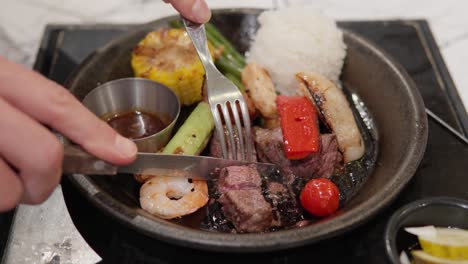 Cutting-Roasted-Beef-Steak-Served-With-White-Rice,-Grilled-Prawns,-And-Vegetables