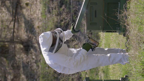 VERTICAL,-SLOW-MOTION---Beekeeper-smokes-beehives-to-prevent-aggression,-slowmo-wide-shot