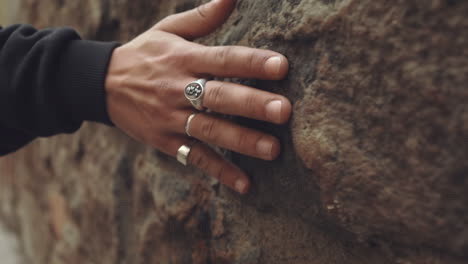 Caucasian-hands-with-silver-rings-drag-along,-feeling-the-stone-wall