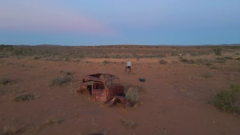 Aerial-Orbit-view-Male-photographer-taking-photos-of-old-rusty-Abandoned-car-on-Outback