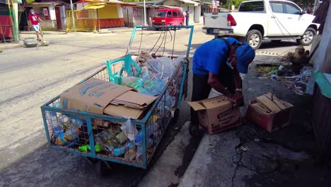 An-old-man-scavenging-plastic-bottles,-paper-boxes,-and-scrap-metal-beside-the-street-under-the-sun