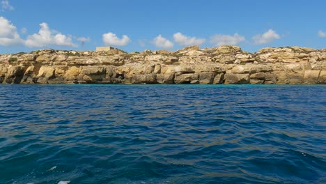 Low-angle-sea-level-view-from-sailing-boat-of-Favignana-island-and-turquoise-sea-water-in-Sicily,-Italy