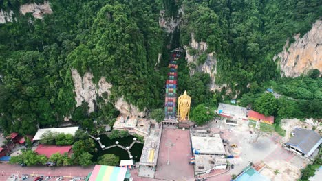 Luftdrohne-Umkreist-Die-Großen-Kalksteinberge-Der-Batu-Höhlen-In-Kuala-Lumpur,-Malaysia,-Mit-Einer-Farbenfrohen-Treppe,-Die-An-Einem-Bewölkten-Nachmittag-Und-Ohne-Touristen-Zur-Lord-Murugan-Statue-Führt