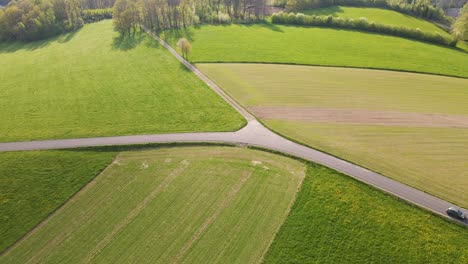 Car-driving-around-a-bend-on-an-open-country-road-through-beautiful,-lush-green-fields-in-the-rural-countryside-of-Germany,-Europe